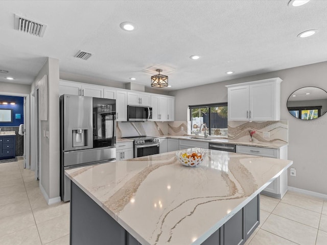 kitchen with sink, stainless steel appliances, light stone counters, white cabinets, and a kitchen island