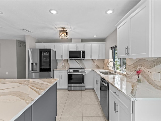 kitchen with sink, light tile patterned floors, stainless steel appliances, light stone countertops, and white cabinets