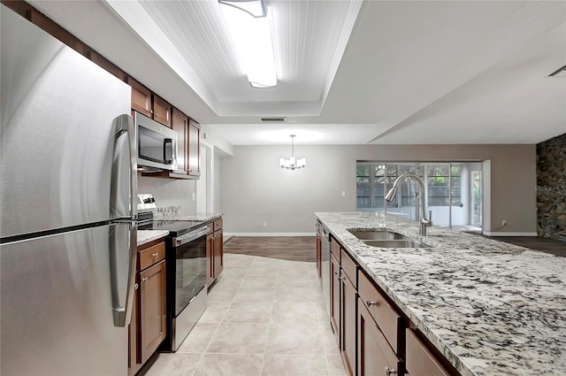 kitchen with sink, decorative light fixtures, light stone countertops, and appliances with stainless steel finishes