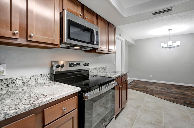 kitchen featuring an inviting chandelier, light tile patterned floors, appliances with stainless steel finishes, pendant lighting, and light stone countertops