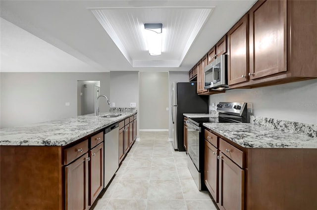 kitchen with light tile patterned flooring, sink, a tray ceiling, stainless steel appliances, and light stone countertops