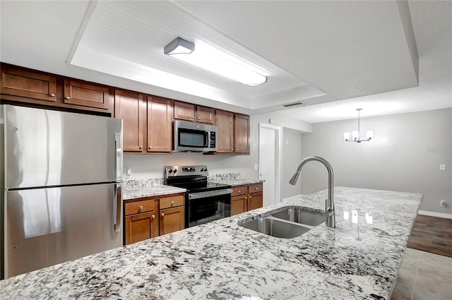 kitchen with a raised ceiling, sink, hanging light fixtures, light stone counters, and stainless steel appliances