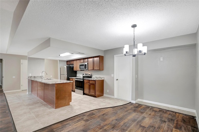 kitchen with pendant lighting, sink, appliances with stainless steel finishes, an island with sink, and light wood-type flooring