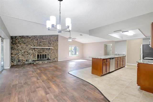 kitchen with a stone fireplace, appliances with stainless steel finishes, a textured ceiling, decorative light fixtures, and vaulted ceiling