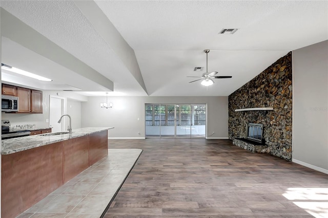 kitchen with sink, ceiling fan with notable chandelier, appliances with stainless steel finishes, light stone counters, and a stone fireplace