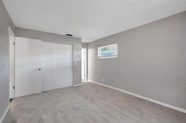 unfurnished bedroom with light colored carpet and a closet