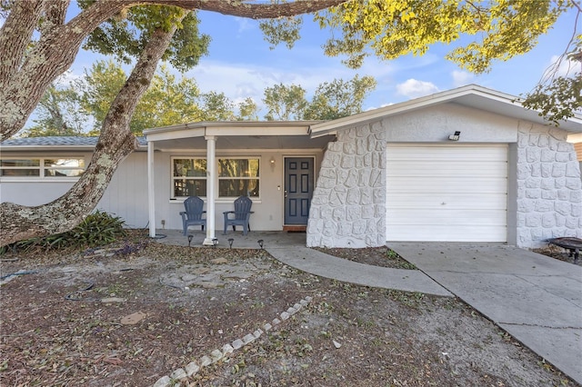 ranch-style home featuring an attached garage, covered porch, driveway, and stone siding