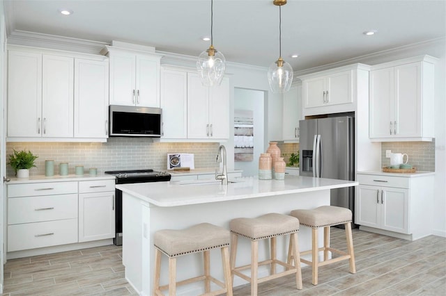 kitchen with appliances with stainless steel finishes, a kitchen island with sink, pendant lighting, and white cabinets