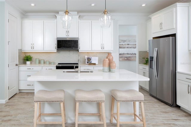 kitchen with white cabinetry, appliances with stainless steel finishes, a center island with sink, and decorative light fixtures