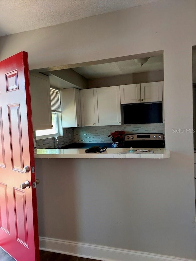 kitchen featuring stainless steel electric range oven, white cabinetry, and tasteful backsplash