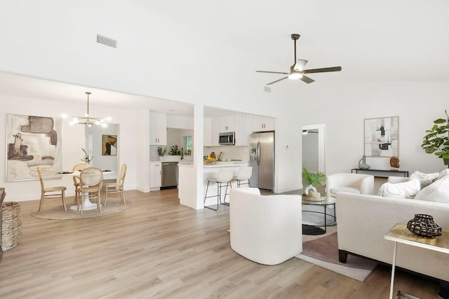 living room with ceiling fan with notable chandelier, high vaulted ceiling, and light wood-type flooring