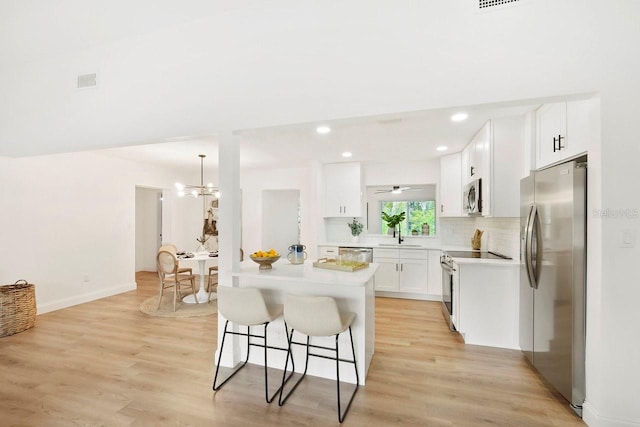 kitchen with white cabinetry, tasteful backsplash, hanging light fixtures, light hardwood / wood-style flooring, and appliances with stainless steel finishes