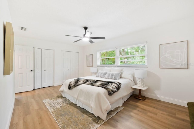 bedroom with two closets, light hardwood / wood-style floors, and ceiling fan