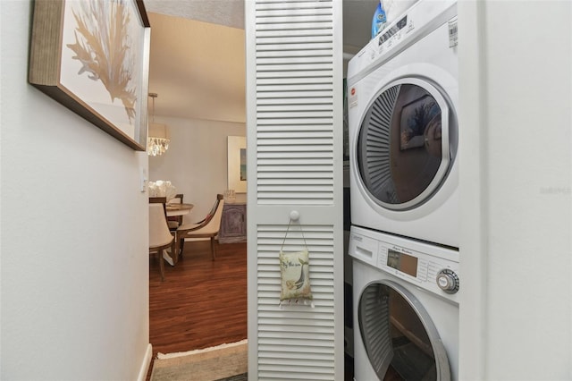washroom with stacked washer and dryer, a chandelier, baseboards, wood finished floors, and laundry area