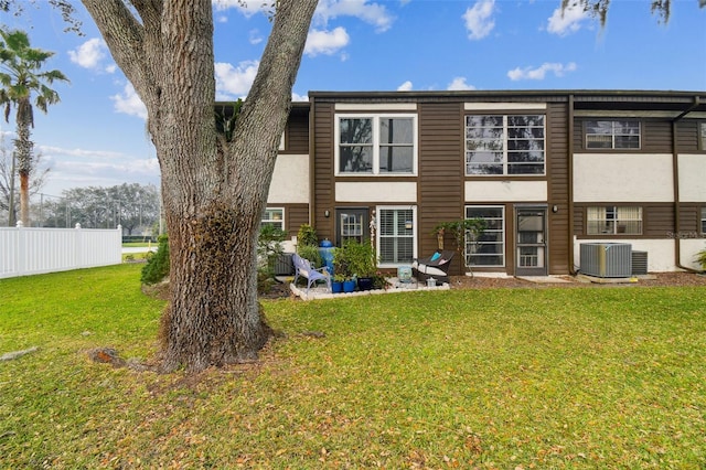 rear view of house with central AC, fence, stucco siding, and a yard