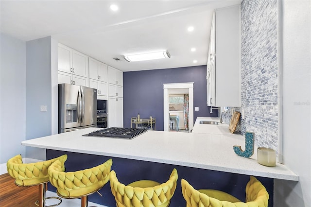 kitchen with stainless steel appliances, kitchen peninsula, a breakfast bar area, and white cabinets