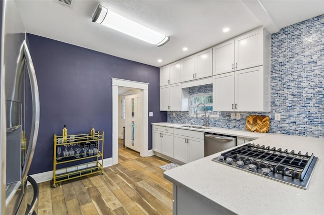 kitchen with sink, tasteful backsplash, stainless steel appliances, light hardwood / wood-style floors, and white cabinets