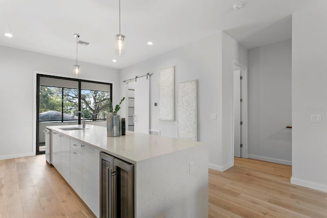 kitchen featuring wine cooler, a center island with sink, hanging light fixtures, white cabinetry, and a sink