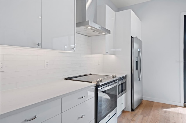 kitchen featuring light countertops, wall chimney range hood, appliances with stainless steel finishes, and white cabinets