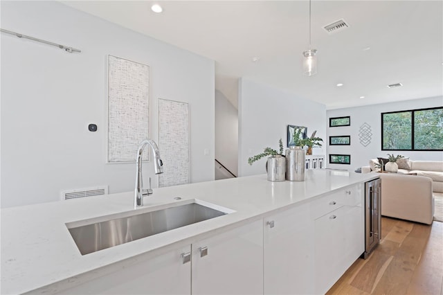 kitchen featuring visible vents, open floor plan, decorative light fixtures, white cabinetry, and a sink