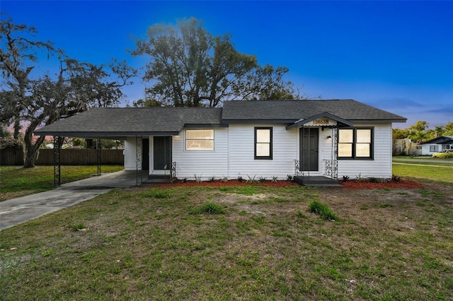 ranch-style home featuring a front lawn, fence, concrete driveway, a shingled roof, and a carport