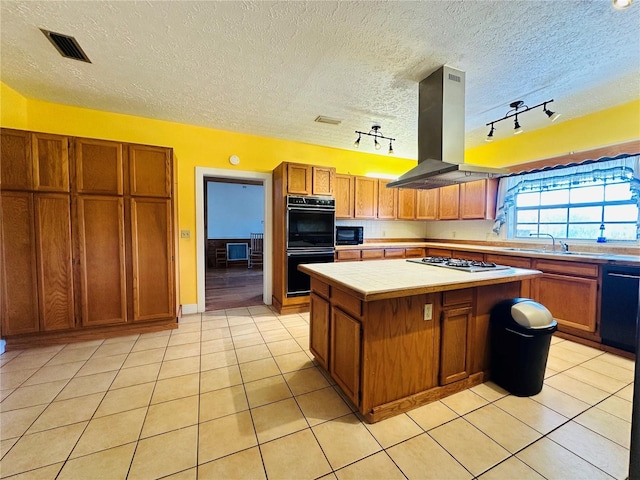 kitchen featuring light tile patterned flooring, island range hood, a center island, tile counters, and black appliances