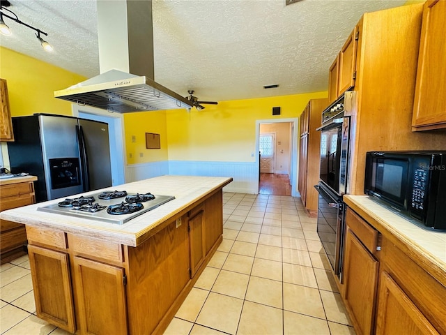 kitchen featuring a center island, island range hood, black appliances, light tile patterned flooring, and tile countertops