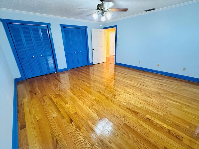 unfurnished bedroom with a textured ceiling, light hardwood / wood-style flooring, ornamental molding, two closets, and ceiling fan