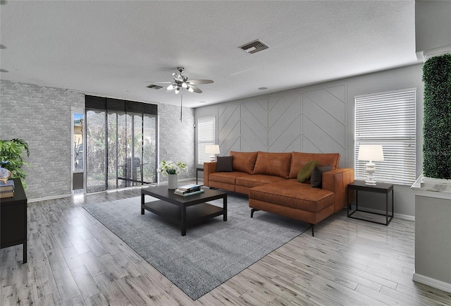 living room featuring ceiling fan, a textured ceiling, and light wood-type flooring