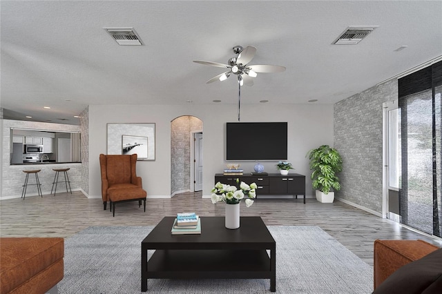 living room with ceiling fan, wood-type flooring, and a textured ceiling