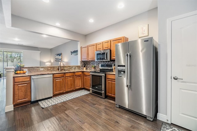 kitchen featuring brown cabinets, stainless steel appliances, decorative backsplash, dark wood-type flooring, and a sink