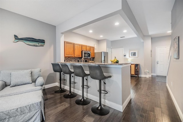 kitchen featuring tasteful backsplash, baseboards, dark wood finished floors, a breakfast bar, and stainless steel appliances