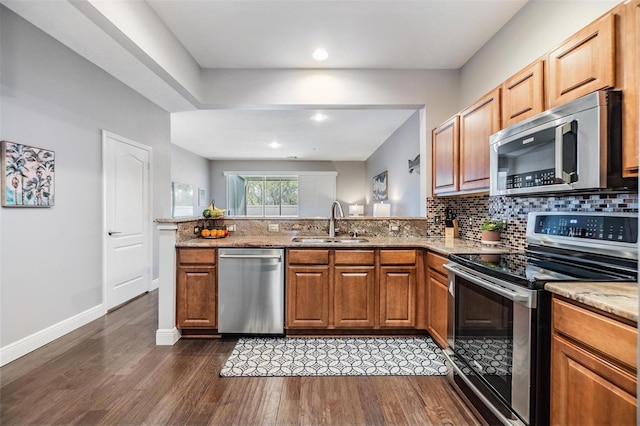 kitchen featuring dark wood finished floors, tasteful backsplash, appliances with stainless steel finishes, a sink, and light stone countertops