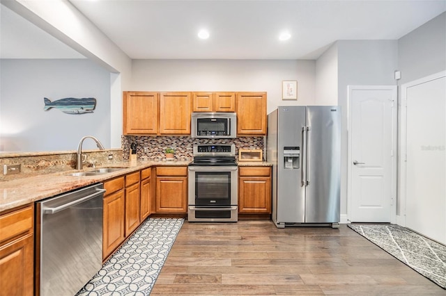 kitchen featuring light wood finished floors, tasteful backsplash, appliances with stainless steel finishes, a sink, and light stone countertops