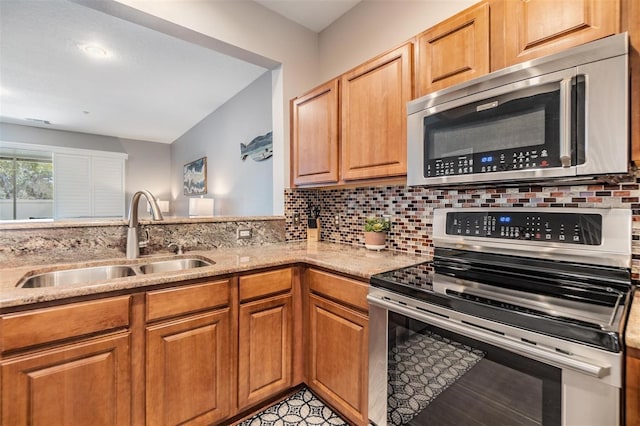 kitchen featuring light stone countertops, a sink, appliances with stainless steel finishes, brown cabinets, and tasteful backsplash