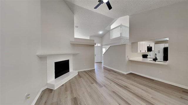 unfurnished living room featuring high vaulted ceiling, sink, ceiling fan, light hardwood / wood-style floors, and a textured ceiling