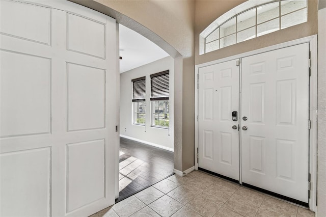 foyer featuring arched walkways, light tile patterned floors, and baseboards