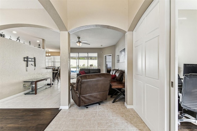 living area with arched walkways, ceiling fan, baseboards, and light tile patterned floors