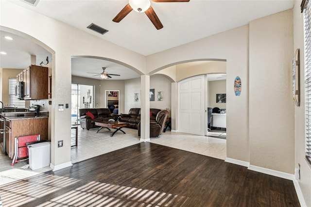 foyer with baseboards, visible vents, arched walkways, a ceiling fan, and light wood-style floors