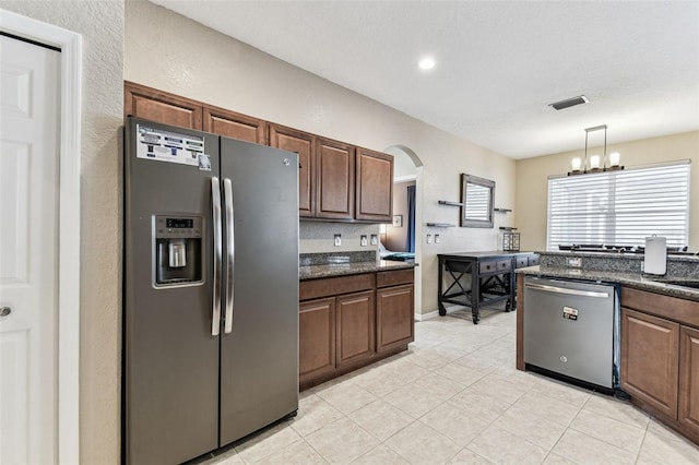 kitchen featuring arched walkways, light tile patterned floors, stainless steel appliances, visible vents, and pendant lighting