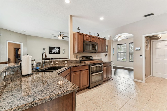 kitchen with arched walkways, stainless steel appliances, a sink, visible vents, and dark stone countertops