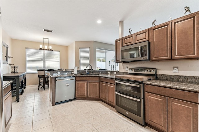 kitchen with light tile patterned floors, stainless steel appliances, a peninsula, a sink, and visible vents