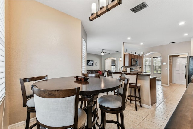 dining area with arched walkways, ceiling fan, light tile patterned floors, visible vents, and baseboards