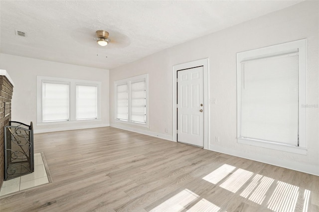 unfurnished living room with ceiling fan, a fireplace, a textured ceiling, and light wood-type flooring