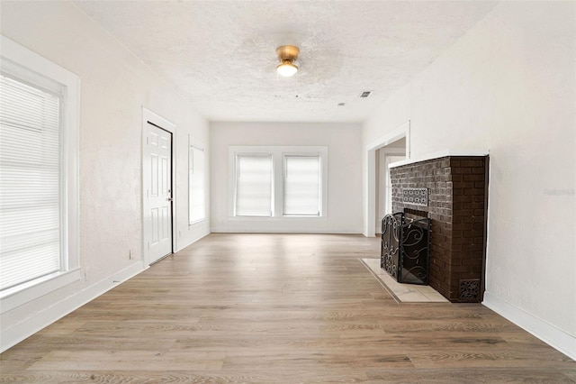 unfurnished living room with a fireplace, a textured ceiling, and light wood-type flooring