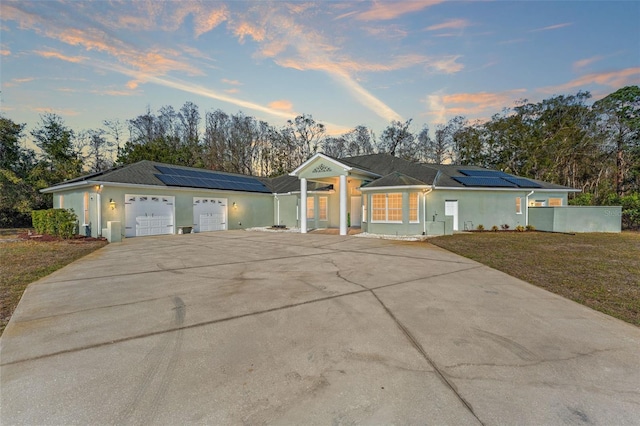 ranch-style home with a garage, a lawn, and solar panels