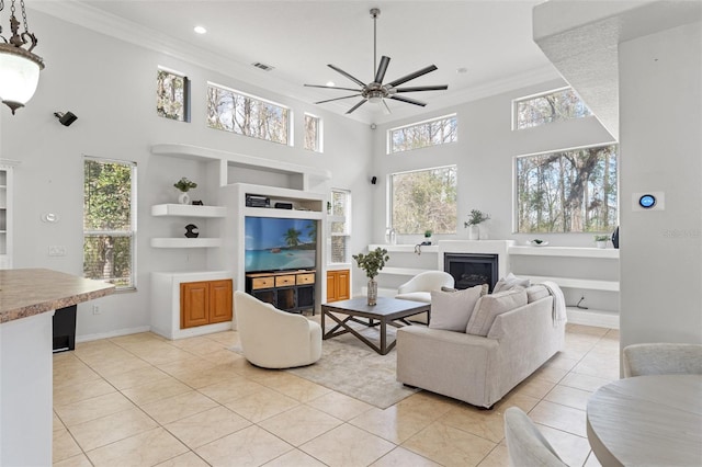 living room featuring built in shelves, crown molding, light tile patterned floors, ceiling fan, and a high ceiling