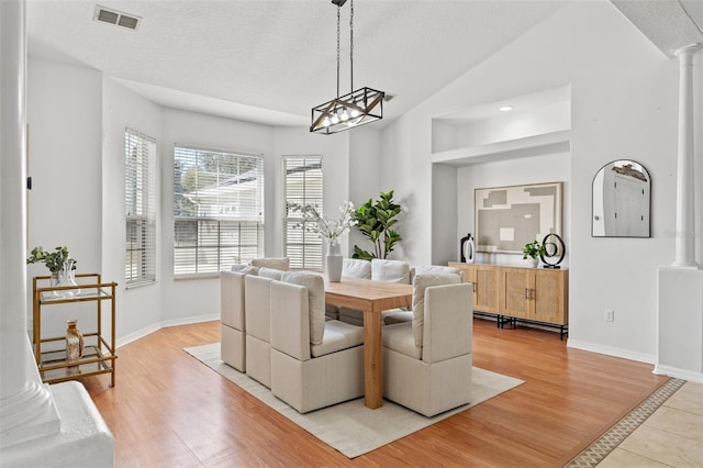 dining space with ornate columns, vaulted ceiling, a textured ceiling, and light wood-type flooring