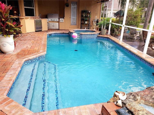 view of swimming pool featuring an outdoor kitchen, a patio, glass enclosure, grilling area, and a pool with connected hot tub