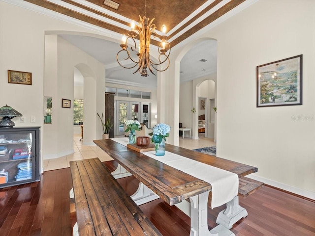 dining space with a tray ceiling, wood-type flooring, ornamental molding, and a chandelier